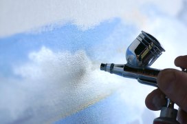 Airbrush being held by fingers near a canvas